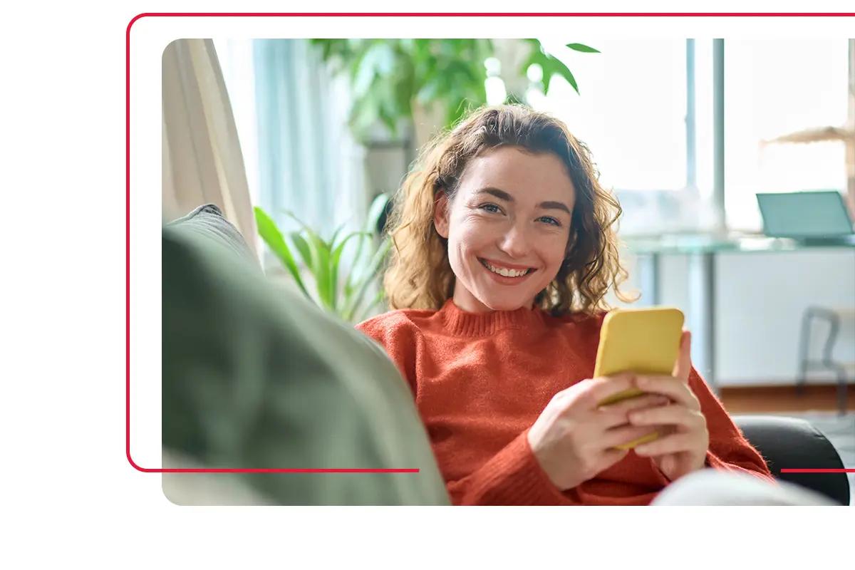 Woman wearing red shirt smiling and sitting on sofa in her apartment that she rents