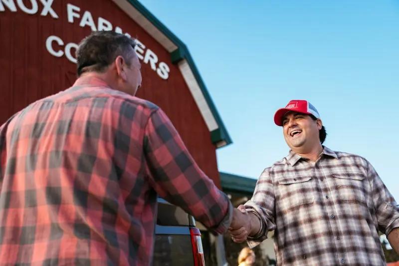 Farm Bureau Insurance of Tennessee agent wearing red hat shaking hands with man outside of Co-Op