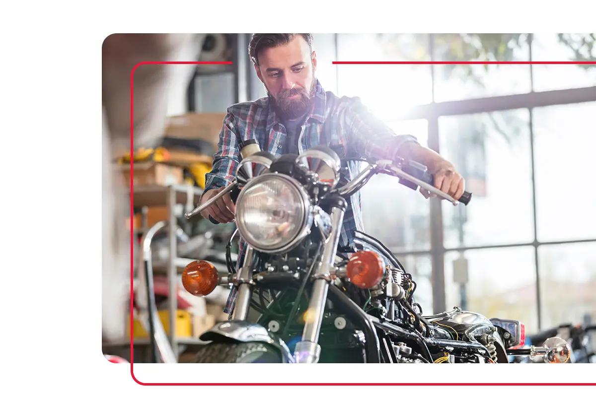 Man with beard and flanel shirt inspecting old motorcycle in motorcycle shop