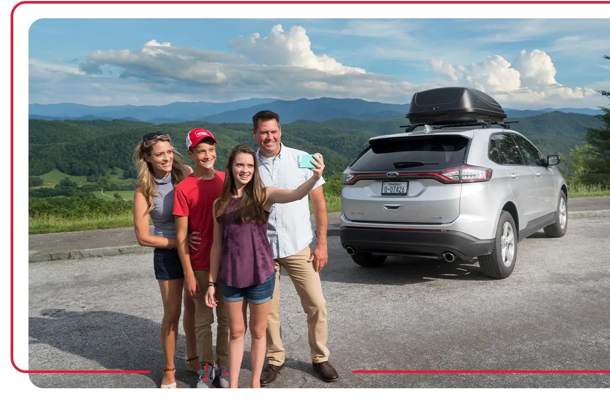Family taking picture next to their silver SUV while overlooking mountains of Tennessee