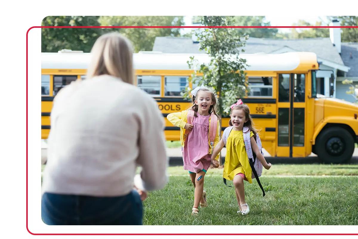 Mother greeting two young daughters as they run from school bus s