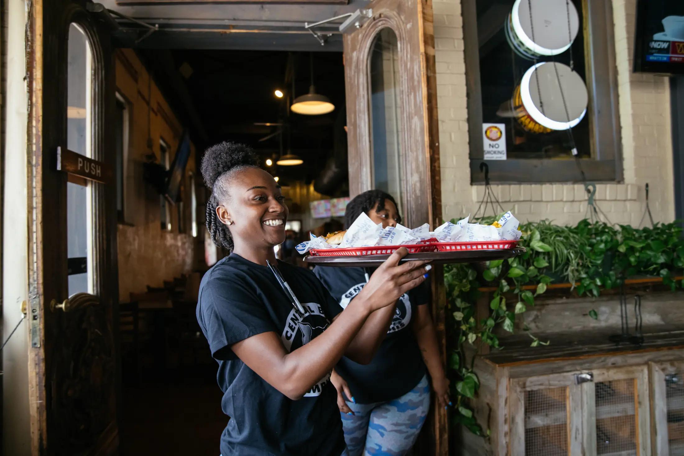 Local restaurant waitress carrying tray of food to diners