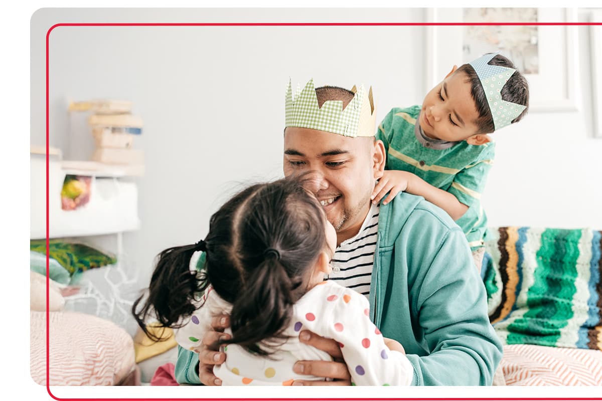 Father playing with his young son and daughter while wearing a craft hat made by the children
